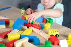 close-up of children's educational toys in hands of toddler, small child, a 2-year-old girl builds houses for characters from color blocks, concept of childhood, earlier child development, creativity
