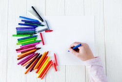 School supplies for drawing on the table: paper and crayons. A child is holding a crayon in his hands