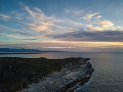 Aerial view of a rocky shore on the Atlantic Ocean Coast during a vibrant sunny sunset. Taken in Cow Head, Newfoundland, Canada.