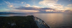Aerial panoramic view of a rocky shore on the Atlantic Ocean Coast during a vibrant sunny sunset. Taken in Cow Head, Newfoundland, Canada.