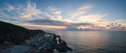 Aerial panoramic view of a rocky shore on the Atlantic Ocean Coast during a vibrant sunny sunset. Taken in Cow Head, Newfoundland, Canada.