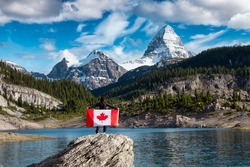 Girl Holding a Canadian National Flag. Beautiful View of Og Lake in the Iconic Mt Assiniboine Provincial Park near Banff, Alberta, Canada. Mountain Landscape