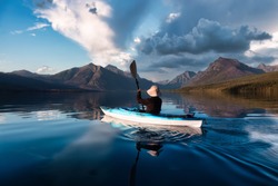 Adventurous Man Kayaking in Lake McDonald with American Rocky Mountains in the background. Colorful Sunset Sky. Taken in Glacier National Park, Montana, USA.
