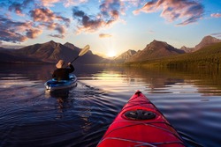 Adventurous Man Kayaking in Lake McDonald with American Rocky Mountains in the background. Colorful Sunrise Sky Art Render. Taken in Glacier National Park, Montana, USA.
