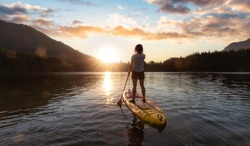 Adventurous Woman Paddling on a Paddle Board in a peaceful lake. Colorful Sunset Art Render. Hicks Lake, Sasquatch Provincial Park near Harrison Hot Springs, British Columbia, Canada.