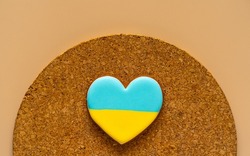Heart shape ukrainian colours blue and yellow national flag gingerbread candy on brown cork texture background.