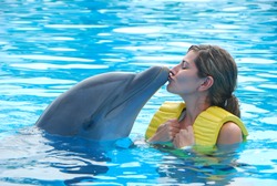Happy woman kissing dolphin in pool