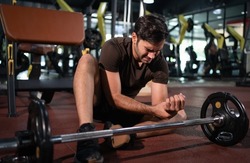 Man feeling pain in his wrist after workout lifting with barbell in fitness gym