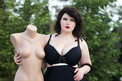 Young beautiful busty curvy  plus size model with big breast in black bra holding mannequin, xxl woman, professional makeup and hairstyle