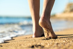 Close up of woman feet walking barefoot on sand leaving footprints on golden beach. Vacation, travel and freedom concept. People relaxing in summer.