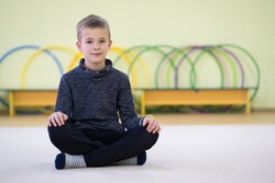 Young child boy sitting and relaxiong on the floor inside sports room in a school after training.