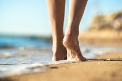 Close up of woman feet walking barefoot on sand beach in sea water. Vacation, travel and freedom concept. People relaxing in summer.