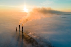 Aerial view of coal power plant high pipes with black smoke moving up polluting atmosphere at sunrise.