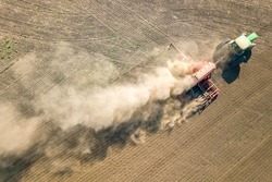Top down aerial view of green tractor cultivating ground and seeding a dry field. Farmer preparing land with seedbed cultivator as part of pre seeding activities in early spring season