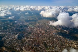 Aerial view from airplane window at high altitude of distant city covered with white puffy cumulus clouds.