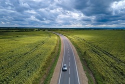 Aerial view of intercity road between green agricultural fields with fast driving car. Top view from drone of highway traffic