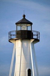 White tall lighthouse on sea shore against blue sky for commercial vessels navigation