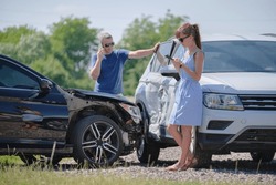 Angry woman and man drivers of heavily damaged vehicles calling insurance service for help in car crash accident on street side. Road safety concept