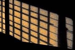 Dark shadow on a stonework wall illuminated by golden sunlight - concept dramatic contrast film noir mystic interior texture background surface structure window close up detail evening sunset sunrise