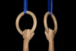Sports, gymnastics: Two male hands grab traditional wooden gymnastic rings tightly in a gym isolated on black background - concept athlete athletics olympics olympic games strength health activity