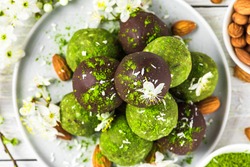 Raw vegan green matcha dessert with matcha energy balls in chocolate glaze and spring flowers. top view. Healthy vegan dessert