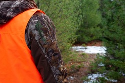 person in camouflage wearing a hunter orange vest to be visible in the woods to hunters 