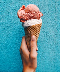 Ice cream cone on a blue background. The woman holding the ice cream by hand.
