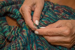 Close up of hands of unrecognizable woman knitting handmade clothes with spokes using  wool yarn. Concept of leisure activity.Knitting from yarn on  coarse spokes.
