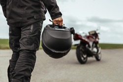 A man walks to his motorcycle, holding a helmet in his hands. Motorcycle helmet close up