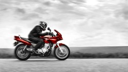 A biker rides a red motorcycle at high speed. Black and white. Selective color effect