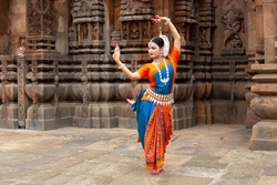 Indian classical Odissi dancer looks at the mirror during the Odissi dance recital against the backdrop of temple sculpture.art and culture of india. 