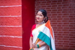 Indian woman in ethnic clothes holding Indian flag on national celebration Independence day or Republic day India against a red brick wall. Incredible India