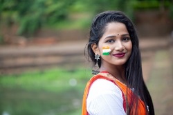 Portrait of a young beautiful female painted tricolor indian flag, tricolour on display by pretty woman to show national pride. Independence day