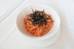 Raw spicy tuna poke appetizer topped with seaweed at a restaurant against a white tablecloth.