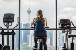Young woman on a stationary bike in a gym on a big city background.