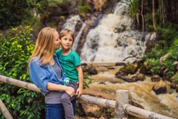 Mom and son on the background of Majestic landscape of waterfall in summer at Dalat, Vietnam