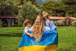Ukrainian mother with two children with flag of Ukraine. Outside. Concept of problem of war in Europe, supporting of families and children, migrants, emigration, patriotism, motherhood, Ukrainian