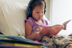 A kid reading in her room with books and listening on her headphones. Children literature and learning how to read.