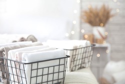 Close-up of white clothes and linen neatly folded in mesh metal containers in bedroom on background of blurred bed. Concept of the perfect organization. Advertising space