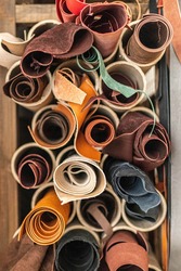 Material for creating handmade production at leather workshop. Selected pieces and bundle of beautiful colored or tanned craftman's work stuff lying inside of cupboard. Storage organization at tannery