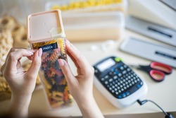 Closeup female hands sticking label on plastic package with pasta. Storage organization of food products keeping. Woman doing housework organize use electronic typing title name case box