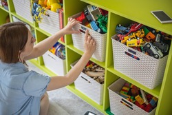 Woman hands applying printing sticker with name title of children toys for comfortable sorting and storage at home. Caring mother organizing domestic space for kids. Housekeeping and household