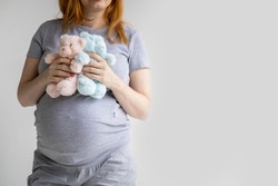 Closeup young pregnant woman hugging two bear toys on huge belly posing isolated on white studio background. Happy future mother tummy enjoying pregnancy awaiting twins baby boy and girl