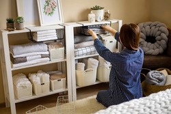 Domestic woman in pajamas neatly putting folded linens into cupboard vertical storage system use Marie Kondo method. Female housewife spring seasonal cleaning space organizer with organized boxes