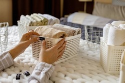 Woman hands neatly folded linens and towels use Marie Kondo method with sticky label tags top view closeup. Female housewife arms sticking names on case box for comfortable storage in bedroom closet