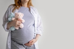 Closeup young pregnant woman hugging two bear toys on huge belly posing isolated on white studio background. Happy future mother tummy enjoying pregnancy awaiting twins baby boy and girl