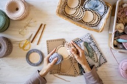 Top view woman hands knitted accessory interior decor use ribbon yarn and wooden stencil pattern on desk table at home. Closeup female arms creating exclusive handmade craft details art work