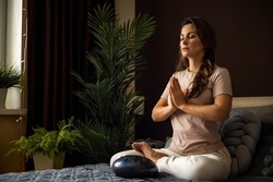 Relaxed yoga woman meditation in lotus position with hands namaste on bed at comfortable bedroom. Spiritual female sitting in front of glucophone percussion drum enjoy balance harmony
