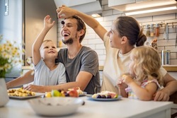Happy family enjoying weekend breakfast together sitting at table with food in kitchen. Smiling father, mother and kids relaxing eating fresh homemade summer dessert waffles with fruits feeling love