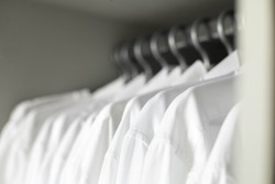 Many white collar clean male shirts on hangers cupboard business clothes storage organization closeup. Man wardrobe fabric textile formal fashion clothing professional monotone uniform garment attire